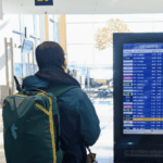 A woman standing in front of a departure board at an airport with a backpack.