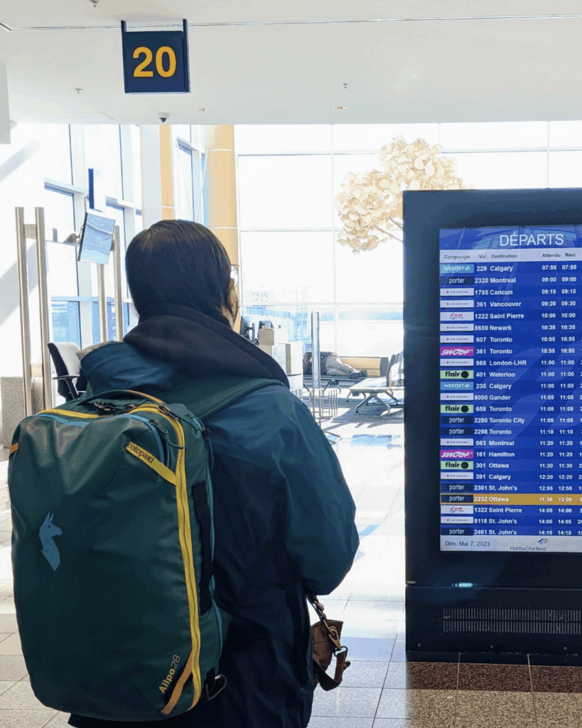 A woman standing in front of a departure board at an airport with a backpack.
